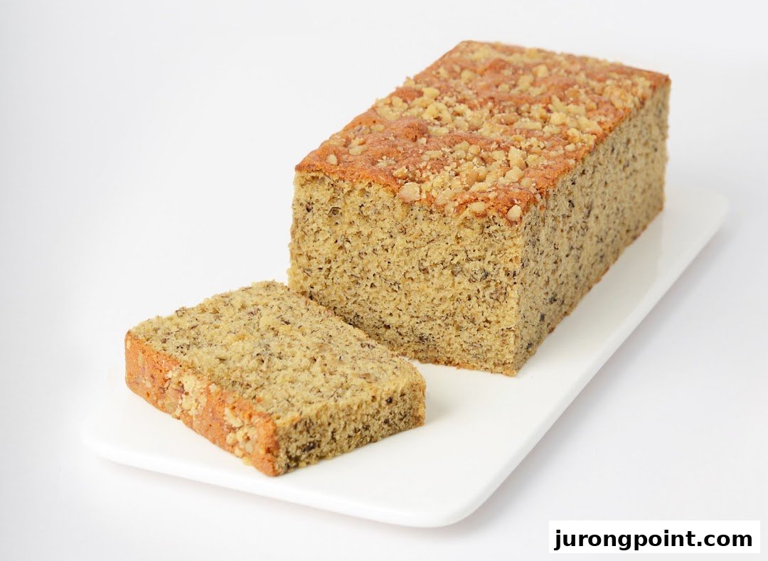 A delicious loaf of banana bread with a slice cut, topped with nuts, on a white platter.