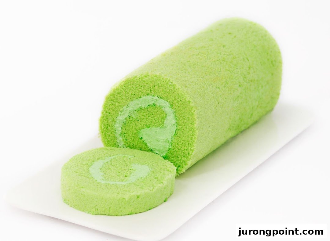 A vibrant green swiss roll cake with a slice cut, displayed on a white plate.