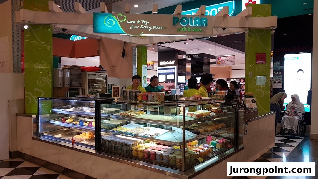 A bustling Polar Puffs & Cakes kiosk in a mall, showcasing a variety of pastries and cakes in display cases.