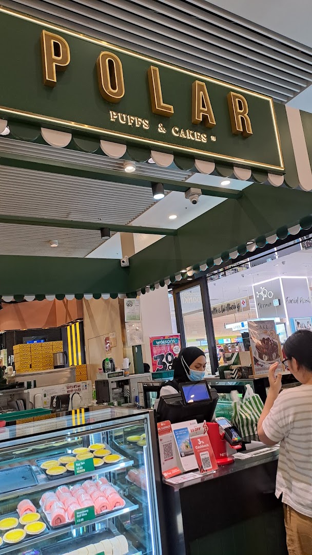 An interior view of Polar Puffs & Cakes, showcasing pastries in a display case and a customer at the counter.