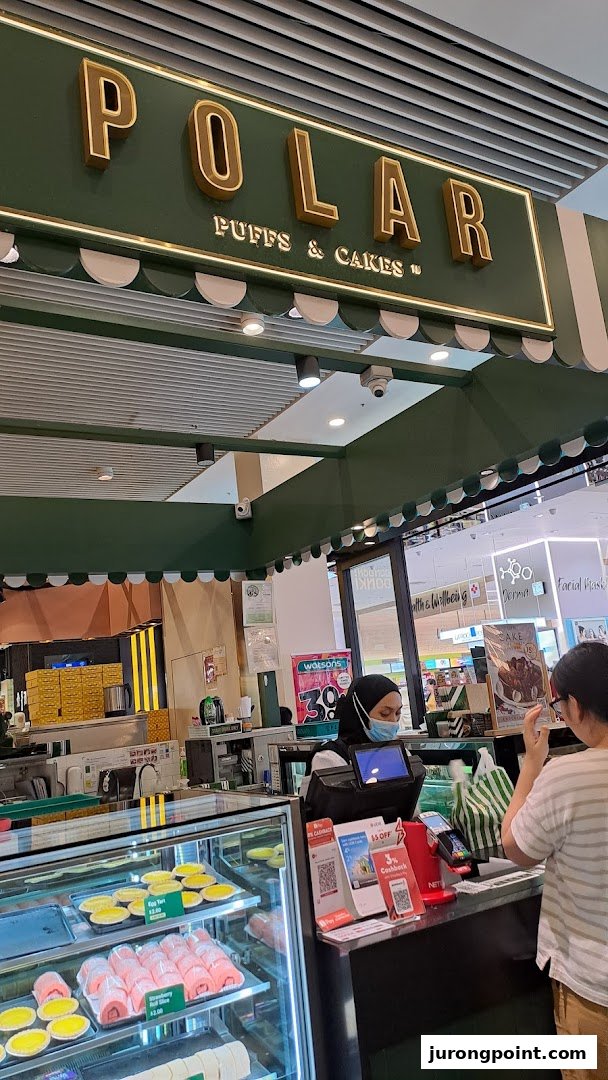 An interior view of Polar Puffs & Cakes, showcasing pastries in a display case and a customer at the counter.
