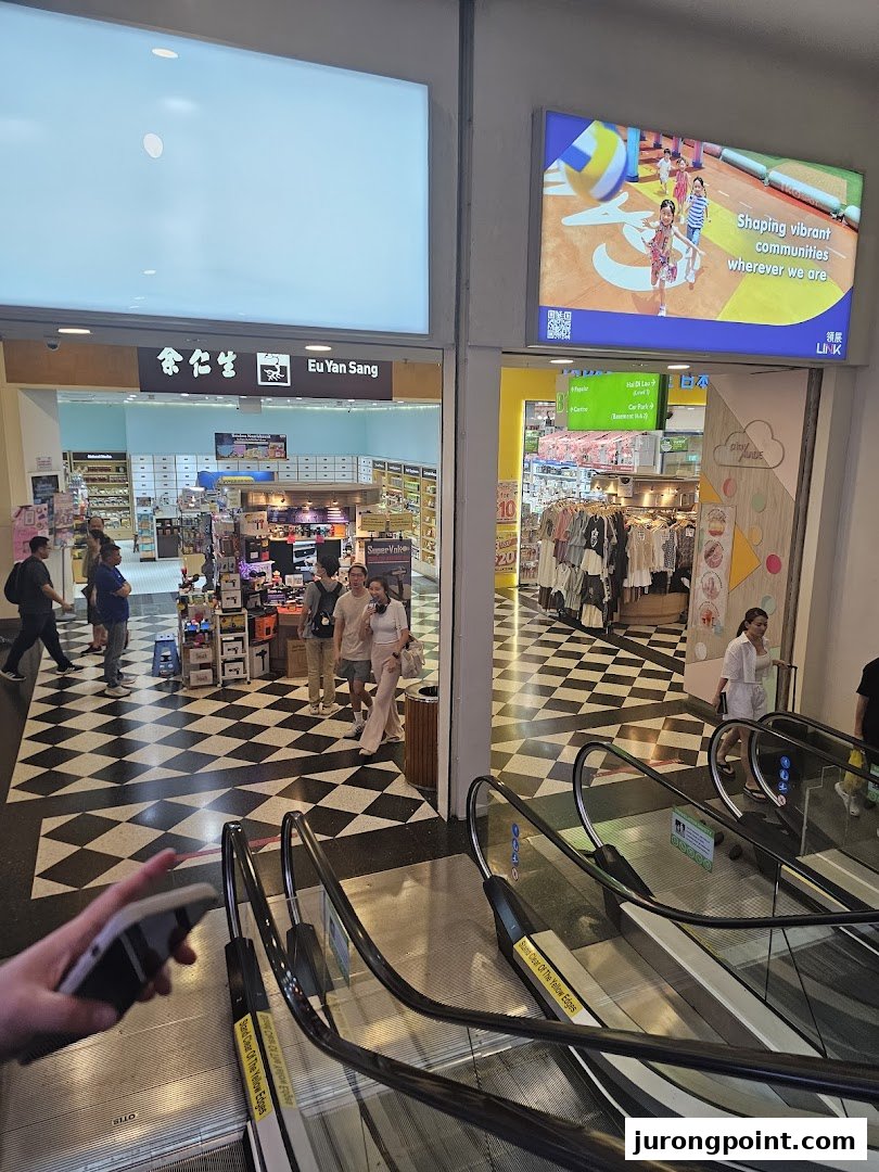 A mall interior showing the entrances of Eu Yan Sang and another retail shop, featuring a distinctive checkered floor and escalators.