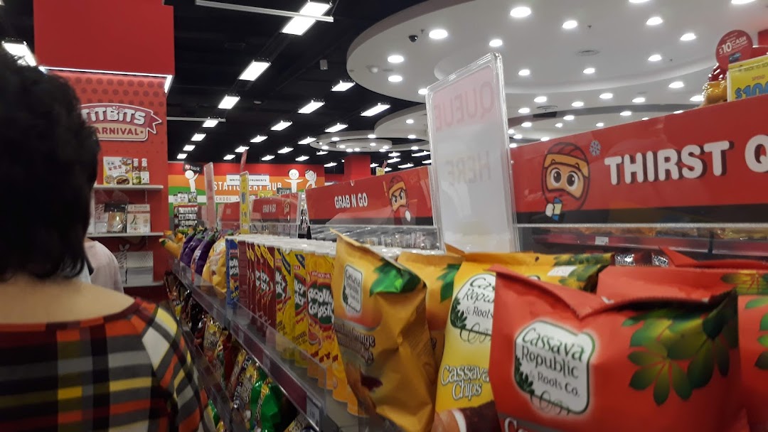 An interior view of a shop aisle featuring snacks and beverages, with a customer browsing.