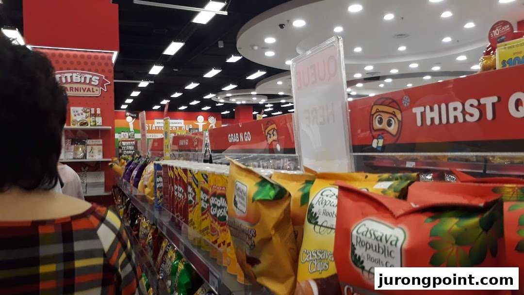 An interior view of a shop aisle featuring snacks and beverages, with a customer browsing.