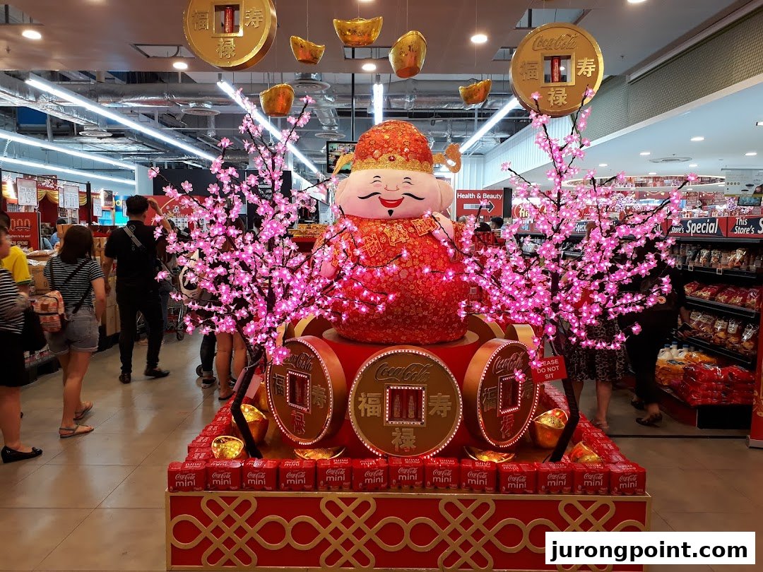 A festive display featuring a large character, pink cherry blossom trees, and Coca-Cola products inside a retail store.