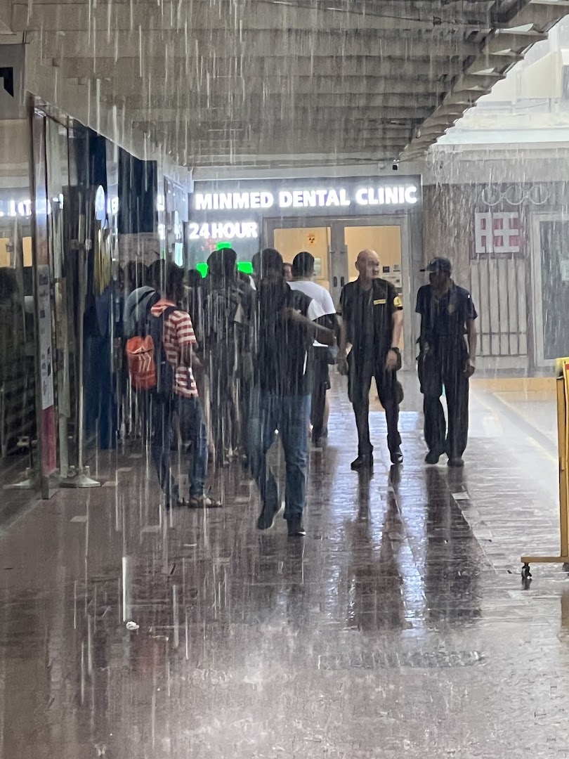 People shelter from heavy rain outside Minmed Dental Clinic, visible with a '24 HOUR' sign.