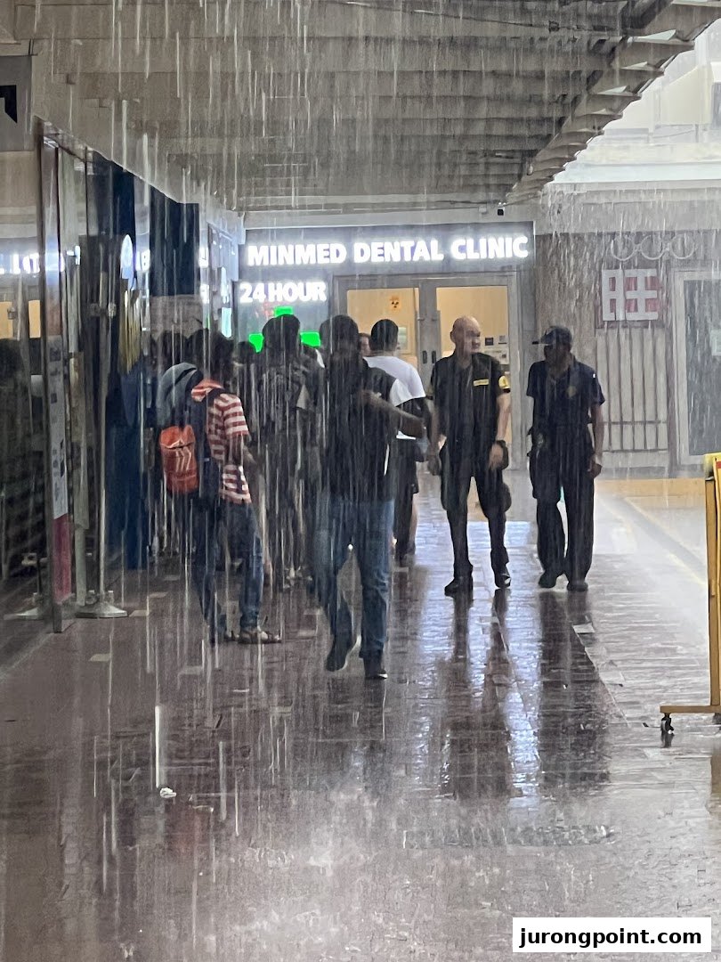 People shelter from heavy rain outside Minmed Dental Clinic, visible with a '24 HOUR' sign.