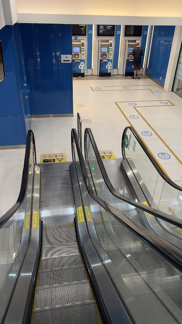 Escalators lead to the POSB Jurong Point ATM lobby, featuring multiple self-service machines and a customer.