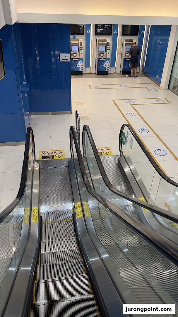 Escalators lead to the POSB Jurong Point ATM lobby, featuring multiple self-service machines and a customer.