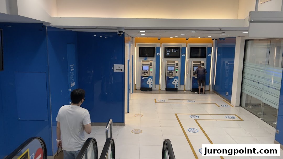 View of the POSB banking area with ATMs and a customer, accessible via escalator.