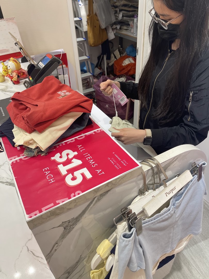 A customer interacts with items at a Purpur clothing store counter during a $15 sale.