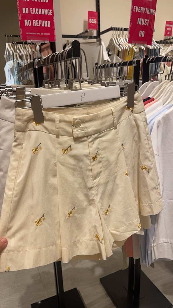 Close-up of cream-colored shorts with yellow embroidery on a hanger in a clothing store.