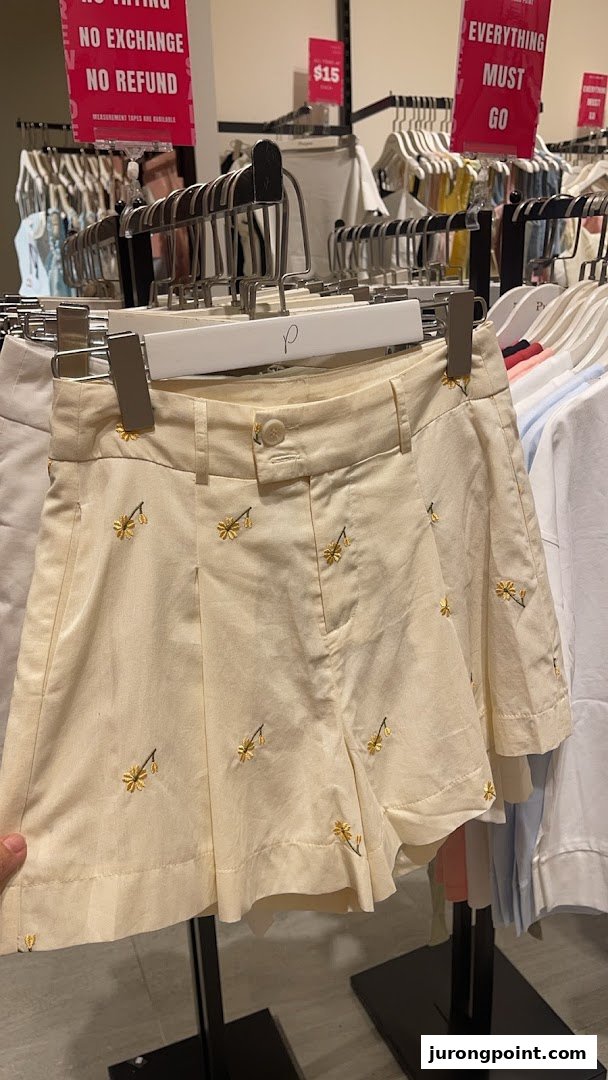Close-up of cream-colored shorts with yellow embroidery on a hanger in a clothing store.