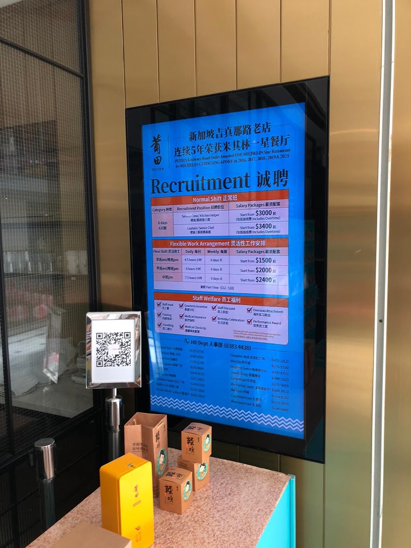 A digital display at PUTIEN showcasing recruitment opportunities and staff welfare benefits, with retail products in the foreground.