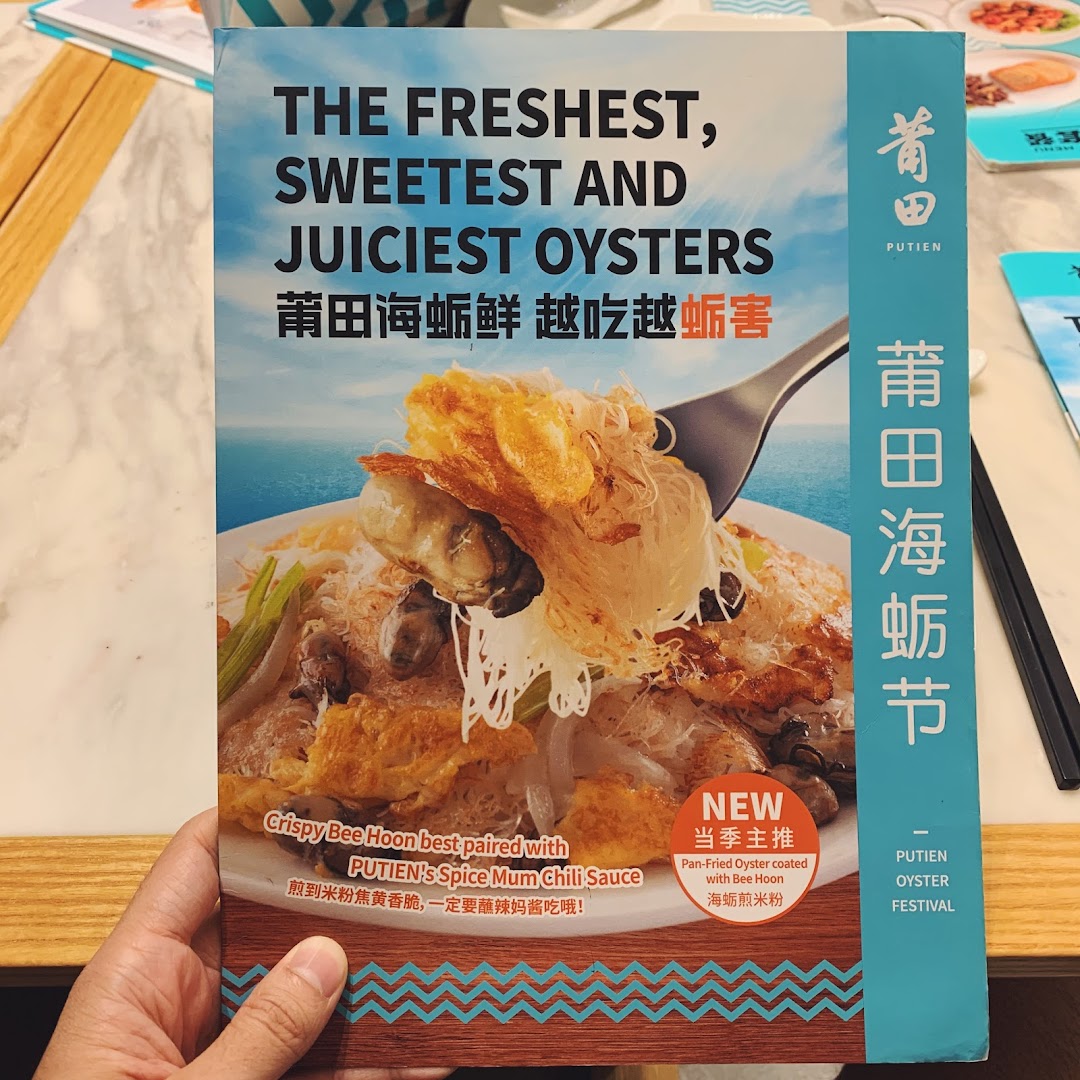 A hand holds a promotional flyer for PUTIEN's Oyster Festival, featuring pan-fried oysters with bee hoon.