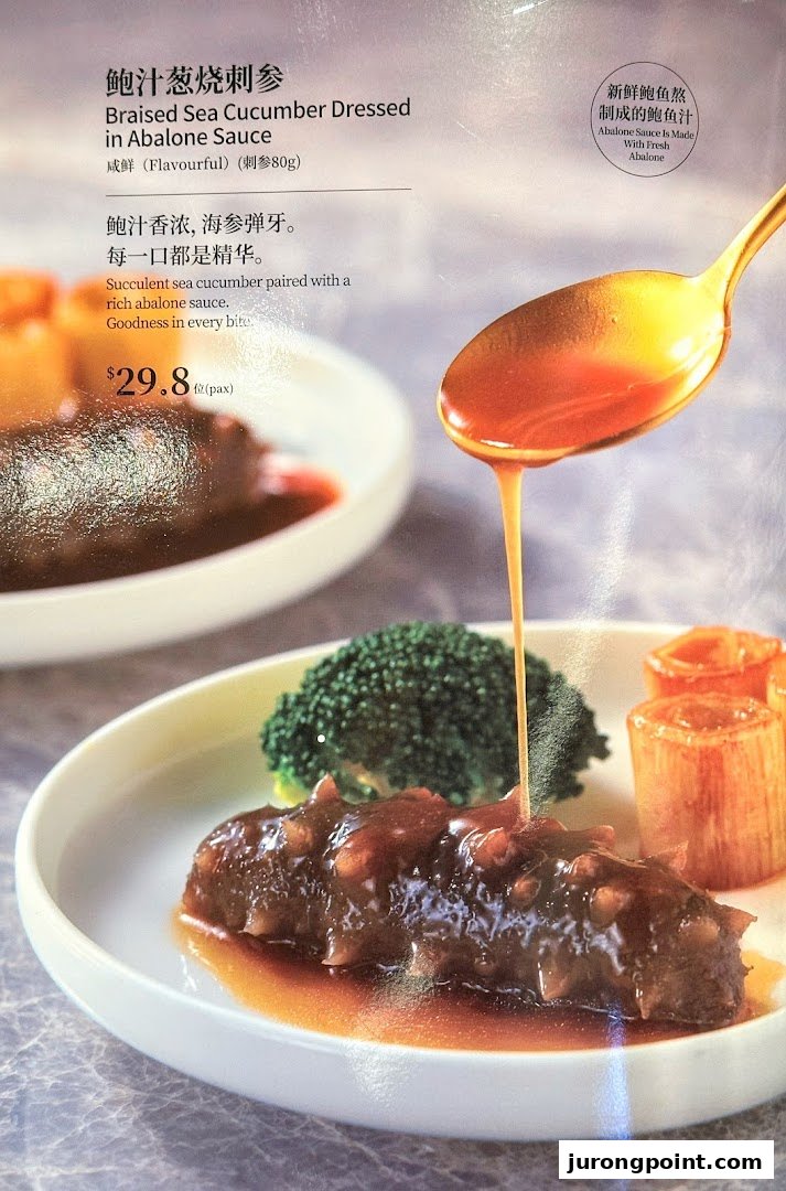 A close-up of Braised Sea Cucumber Dressed in Abalone Sauce with a spoon pouring sauce.
