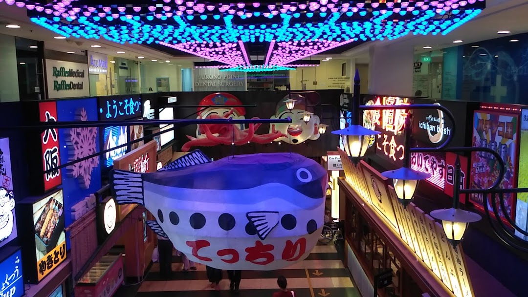 A vibrant mall interior featuring a large inflatable fish, Japanese-themed decor, and various shop signs.