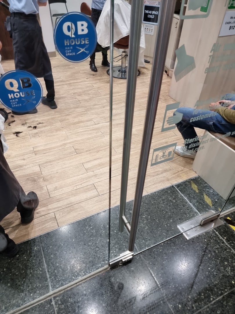View through the glass entrance of QB House, a hair salon, showing staff and customers inside.