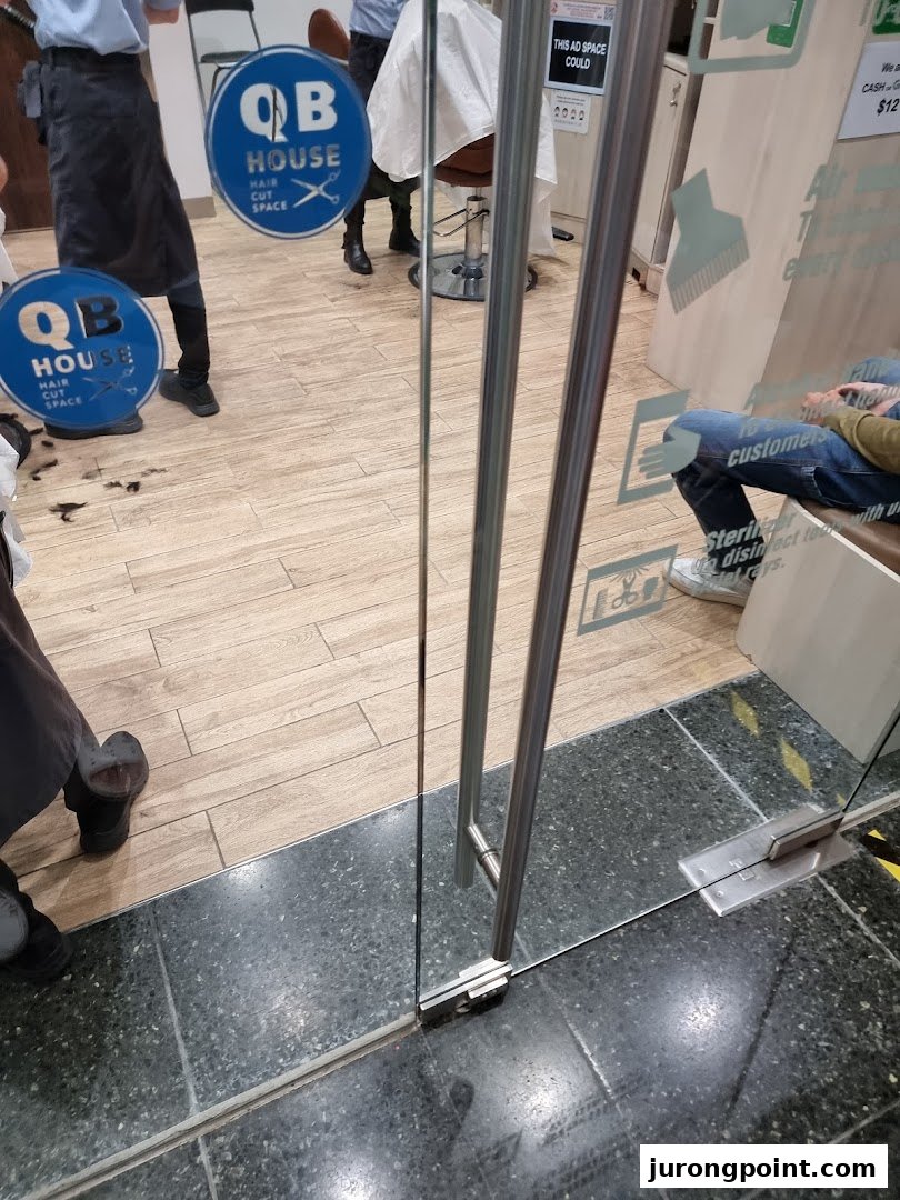 View through the glass entrance of QB House, a hair salon, showing staff and customers inside.
