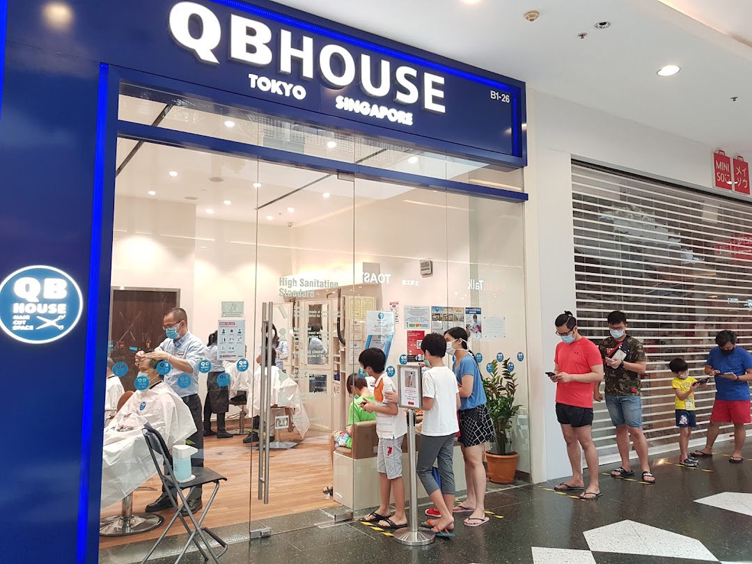 The shop front of QB House, a hair salon, with customers queuing outside for service.