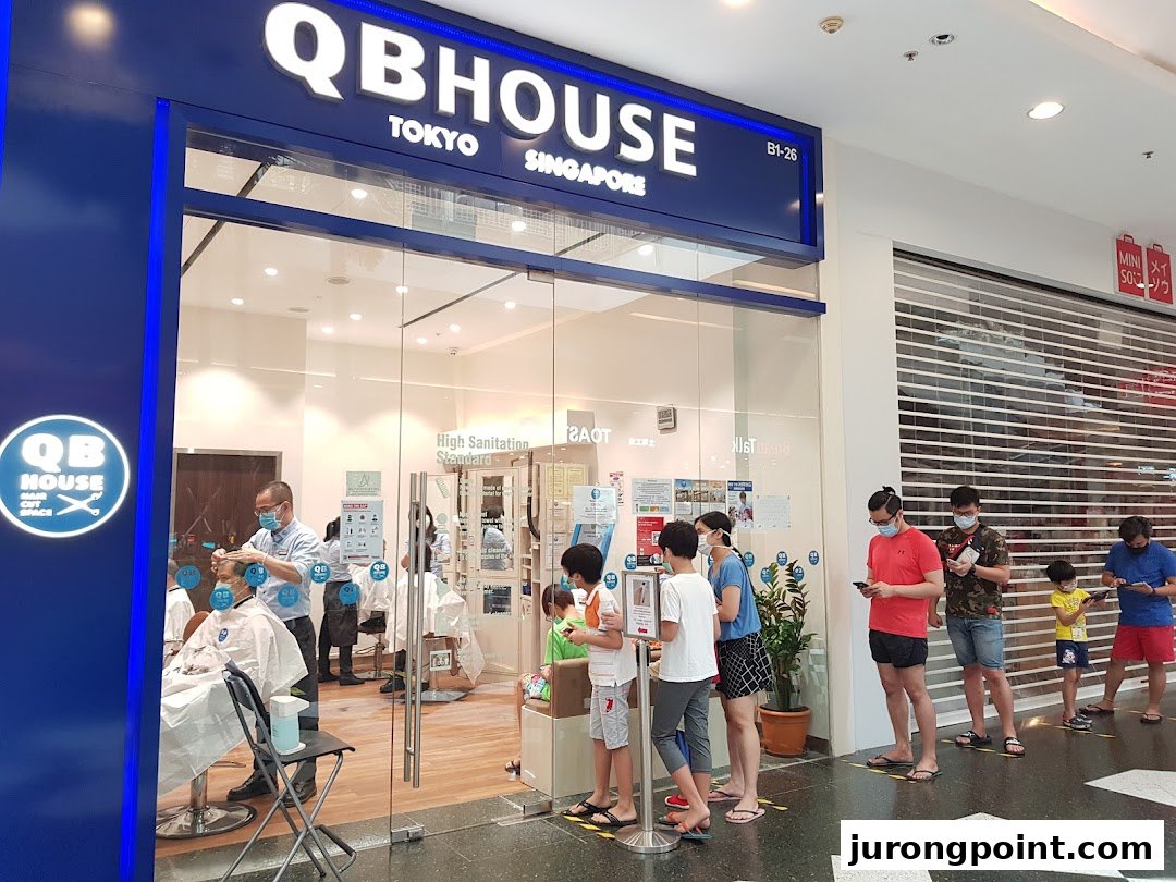 The shop front of QB House, a hair salon, with customers queuing outside for service.