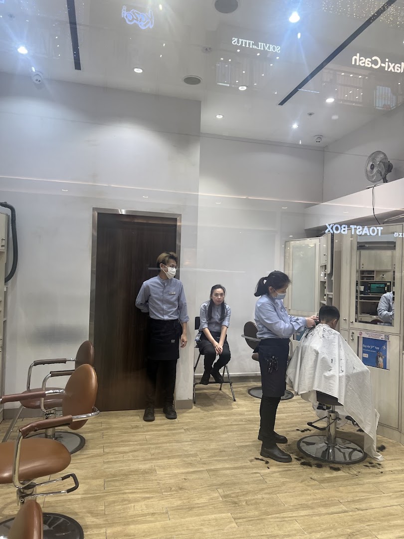 Inside QB House, a barber cuts a customer's hair while staff wait.