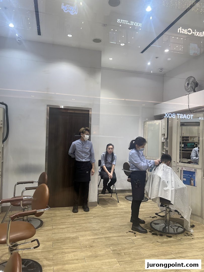 Inside QB House, a barber cuts a customer's hair while staff wait.