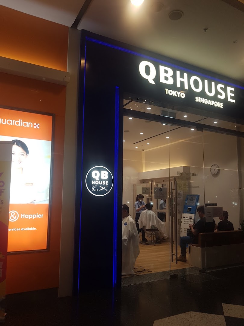 The illuminated entrance of QB House, a hair salon, with customers receiving services inside.