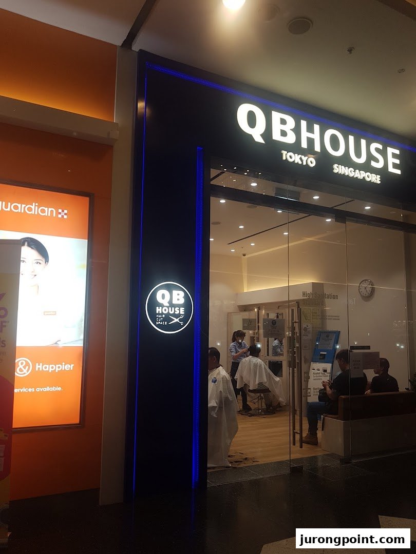 The illuminated entrance of QB House, a hair salon, with customers receiving services inside.