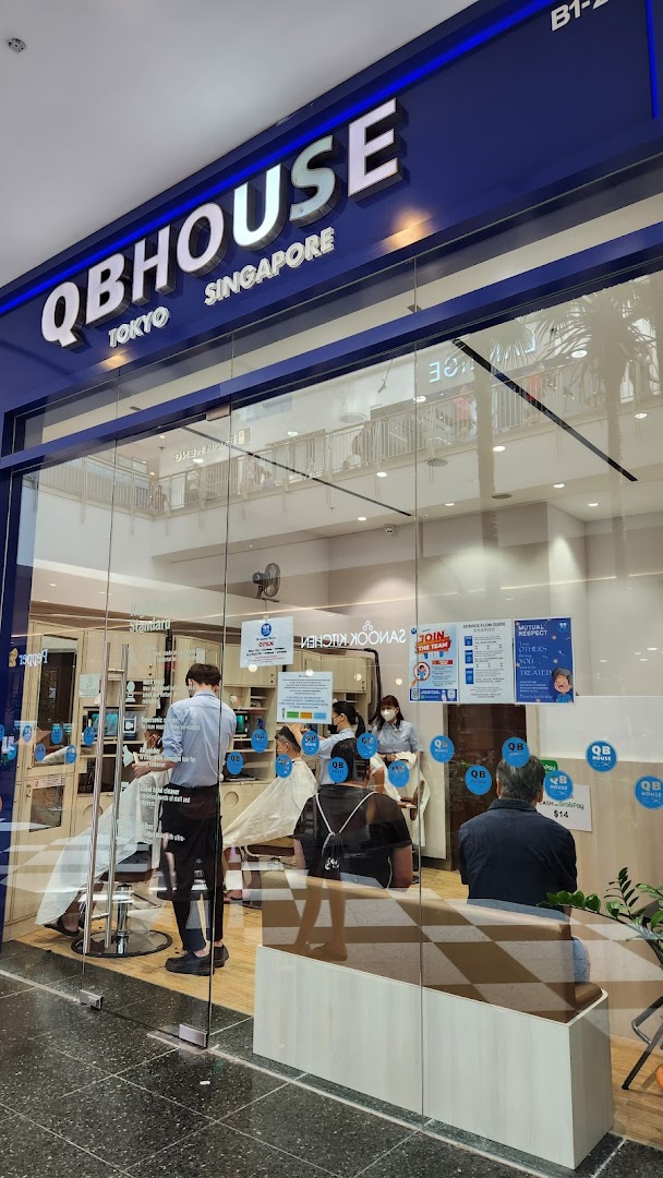 The storefront of QB House, a barbershop, with customers getting haircuts inside.