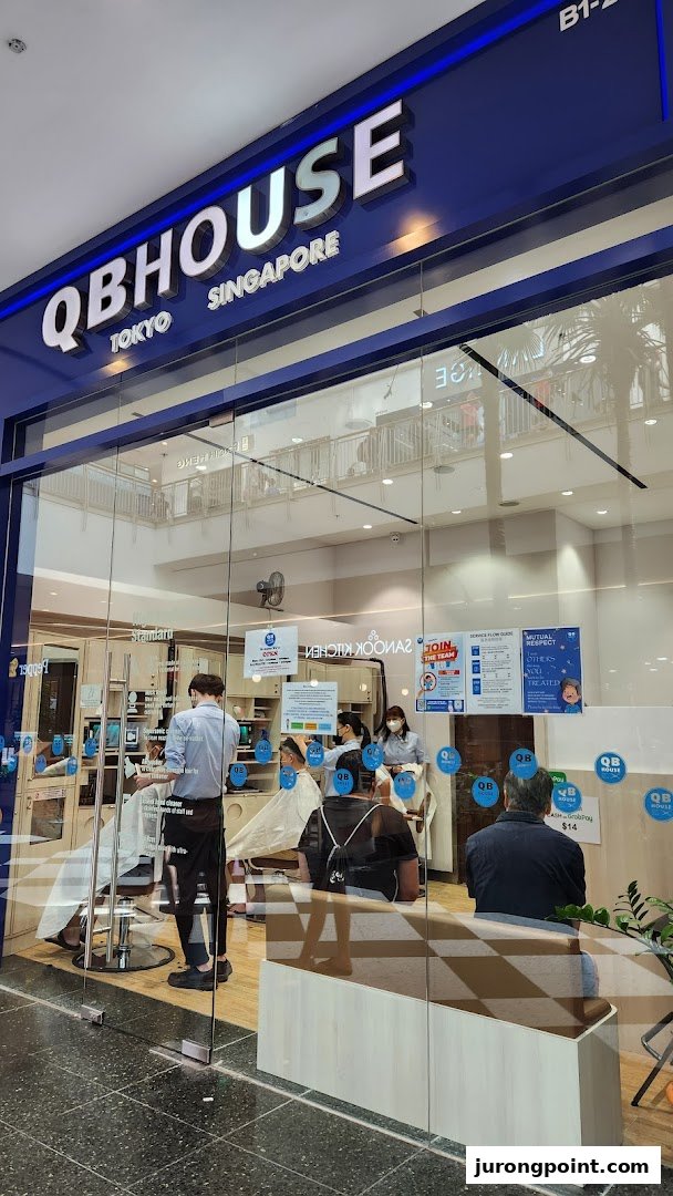 The storefront of QB House, a barbershop, with customers getting haircuts inside.