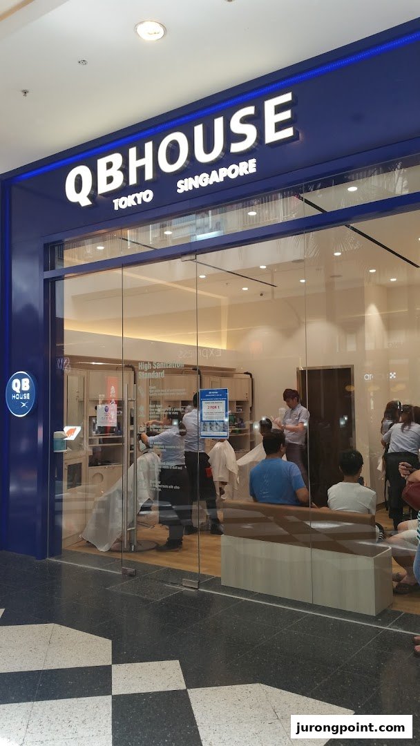 The storefront of QB House, a hair salon, showcasing its interior with customers receiving haircuts.