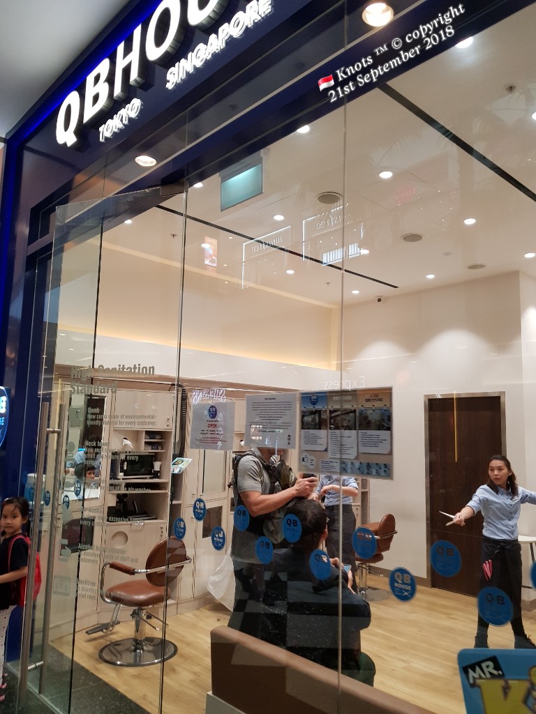 The shop front of QB House, a hair salon, with customers getting haircuts inside.