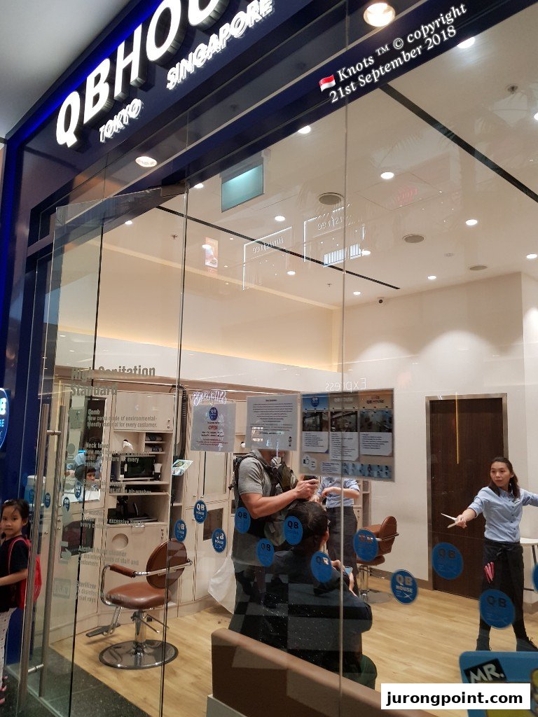 The shop front of QB House, a hair salon, with customers getting haircuts inside.