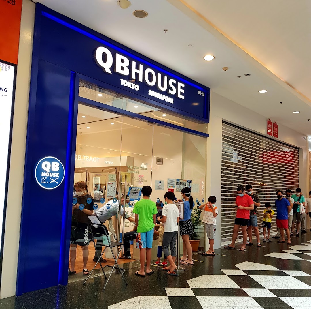 The storefront of QB House, a hair salon, with customers queuing outside.