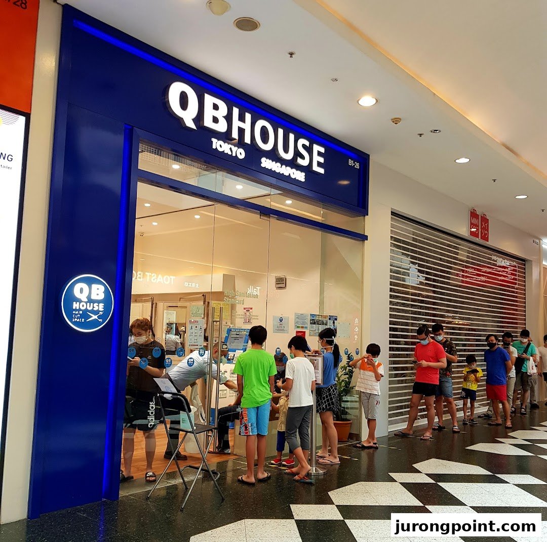 The storefront of QB House, a hair salon, with customers queuing outside.