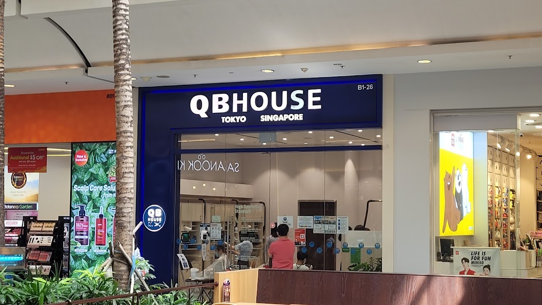 The storefront of QB House, a hair salon, with its prominent blue signage and customers visible inside.