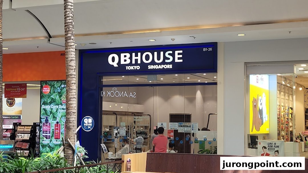 The storefront of QB House, a hair salon, with its prominent blue signage and customers visible inside.