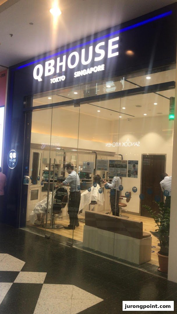 The storefront of QB House, a barbershop, with customers receiving haircuts inside.