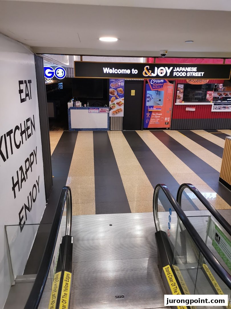 Entrance to &JOY Japanese Food Street from an escalator, featuring various food stalls.