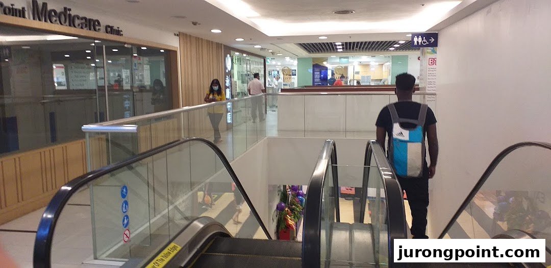 View of an escalator in a shopping mall with clinics and shops visible on the upper level.