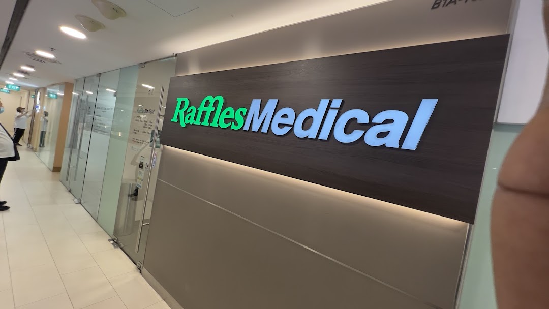 The illuminated sign and glass entrance of Raffles Medical clinic in a shopping mall.