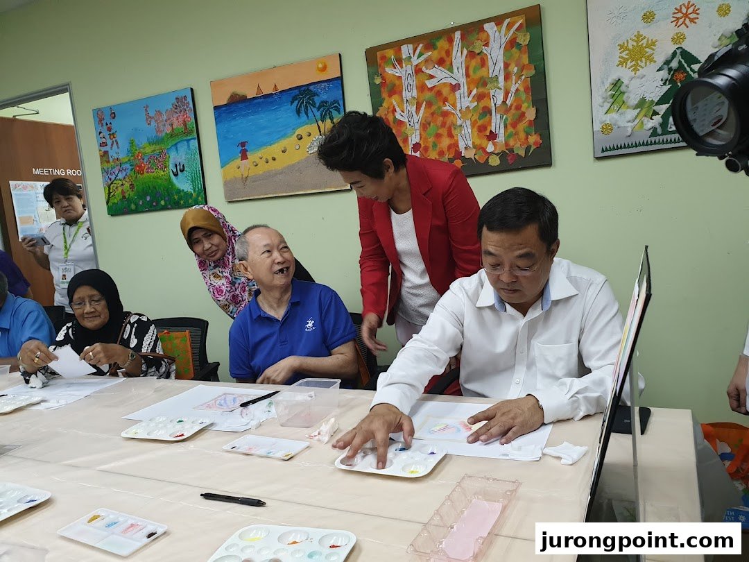 Participants engage in an art activity, painting at tables with palettes, surrounded by colorful artworks.