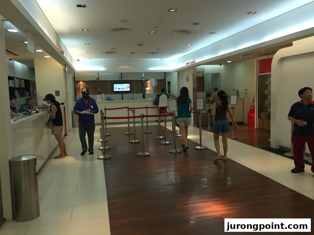 Customers queue and are served at counters inside the Singapore Post Jurong Point branch, offering various postal services.