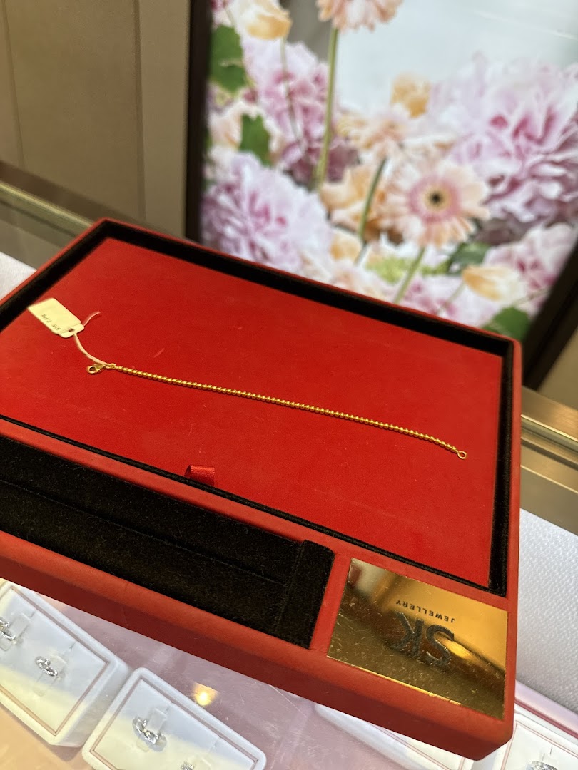 A delicate gold bracelet displayed in a red velvet box at SK Gold.