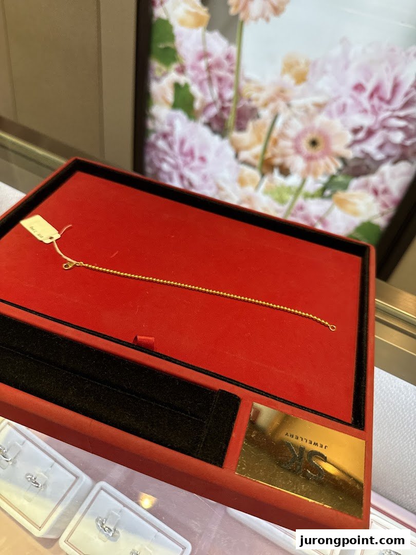 A delicate gold bracelet displayed in a red velvet box at SK Gold.