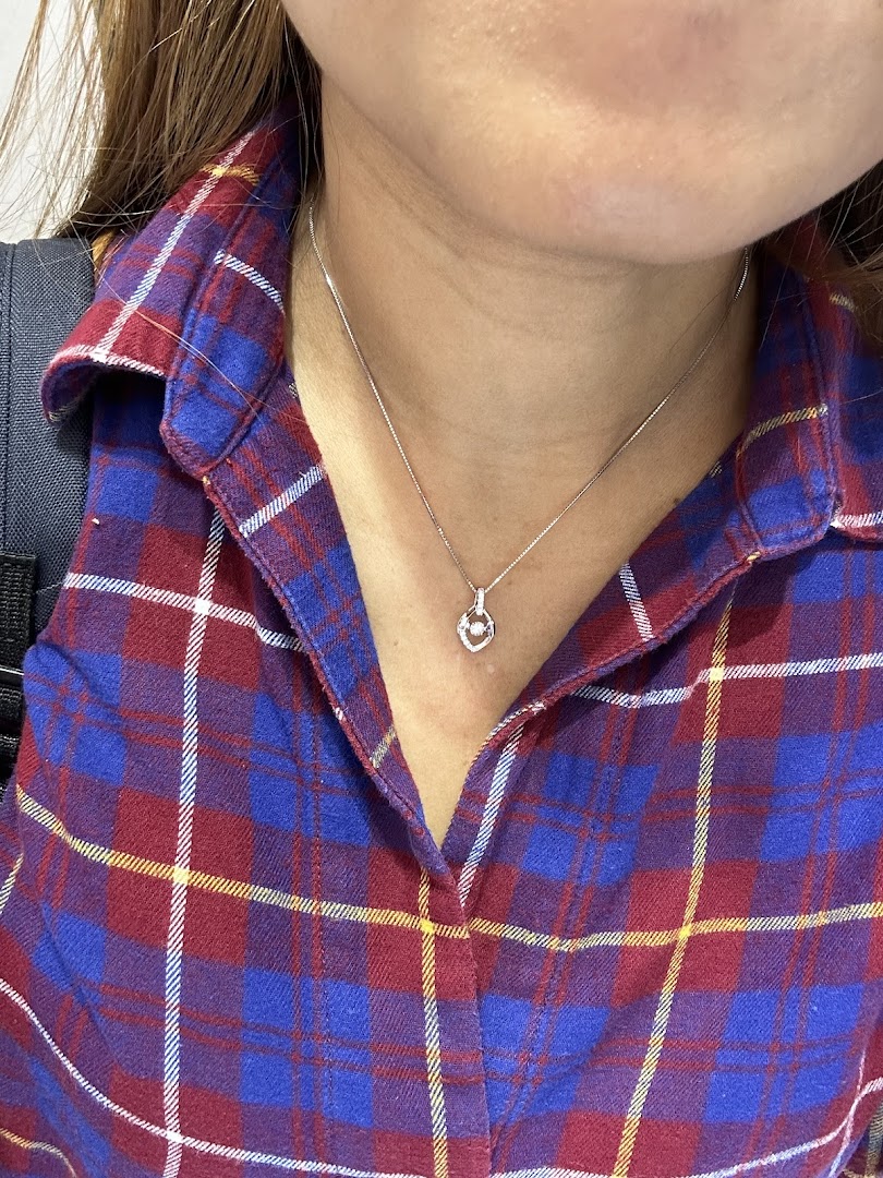A close-up of a person wearing a delicate silver necklace with a heart-shaped pendant and a small gem.