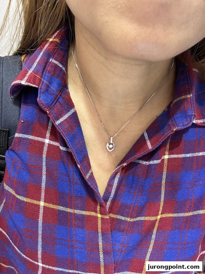 A close-up of a person wearing a delicate silver necklace with a heart-shaped pendant and a small gem.