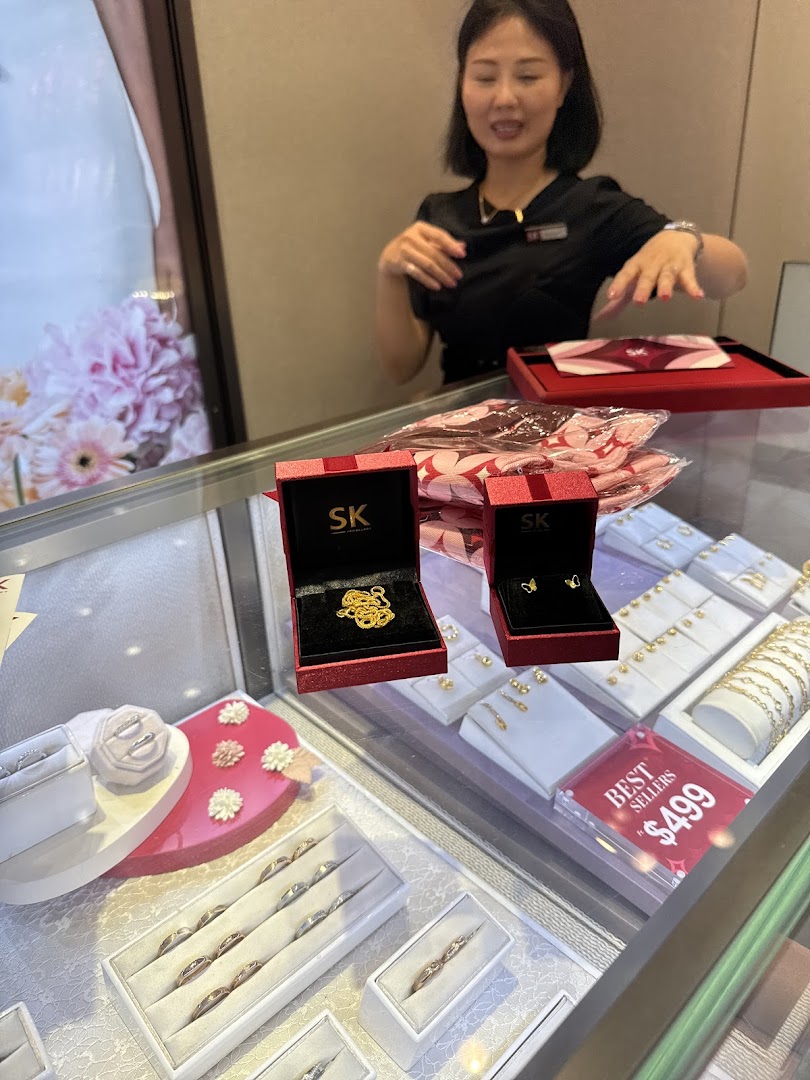 An SK Gold sales associate stands behind a display case showcasing various gold jewelry pieces and branded boxes.