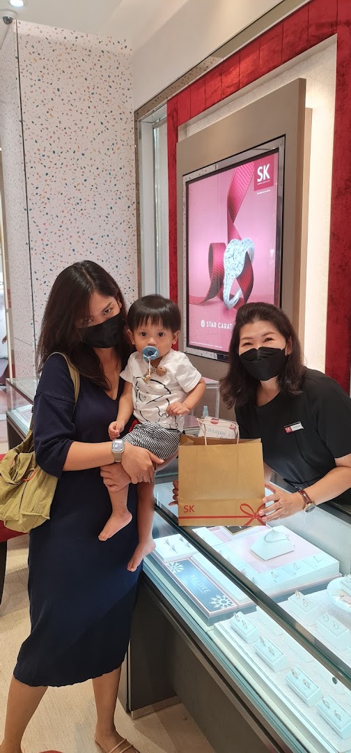 A customer with a baby and a staff member interact inside the SK Gold jewelry store.